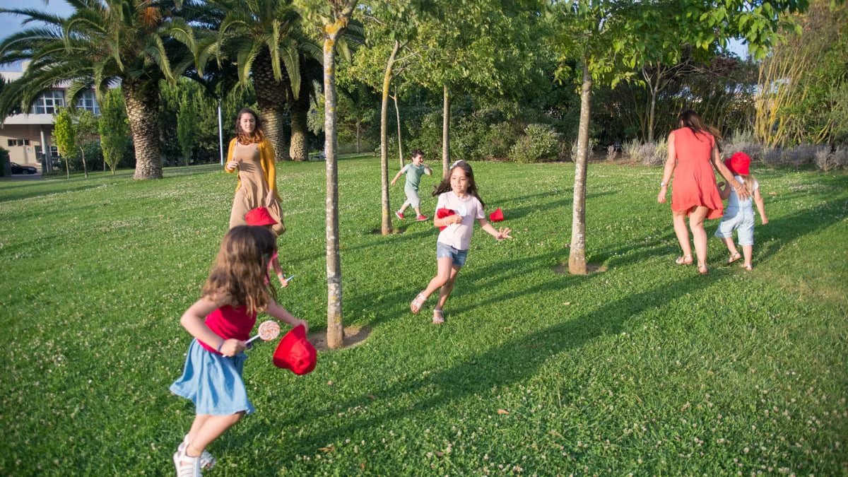 Kids and adults enjoy playing together in a lush, sunny park setting.