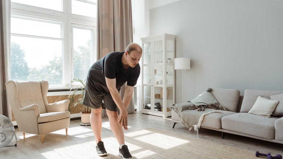 Man performing a stretching exercise in a sunlit living room, embracing a healthy lifestyle.
